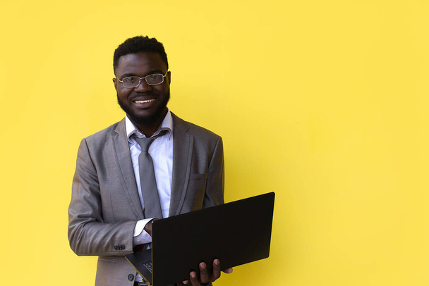 una imagen del joven africano emocionado feliz aislado sobre fondo amarillo usando el ordenador portátil. - Foto, Imagen