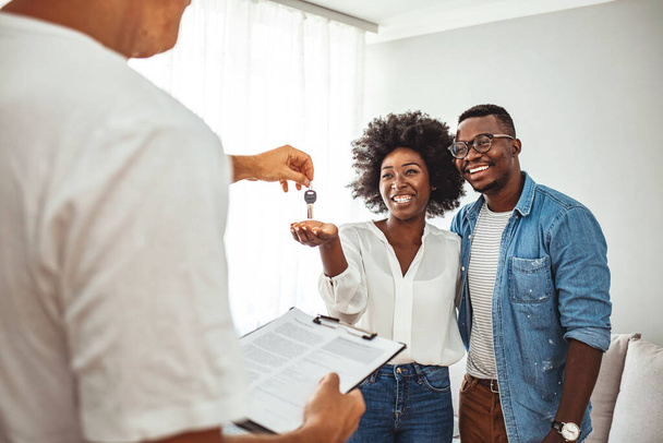 Handsome realtor is giving key to the new apartment to happy young couple. Couple buying new apartment.  A young couple receive the keys to their new apartment from a letting agent. - Photo, image