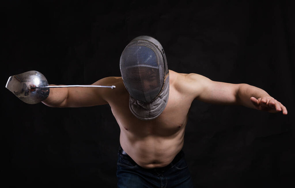 Matured man with naked muscular torso in fencing helmet and epee - Zdjęcie, obraz