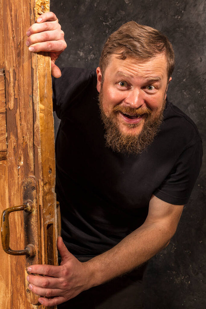 Cheerful bearded man peering out of the door - Fotó, kép