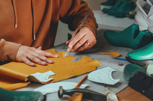 Обувщик резки узоры с помощью ножа из кожи в своей мастерской. - Фото, изображение