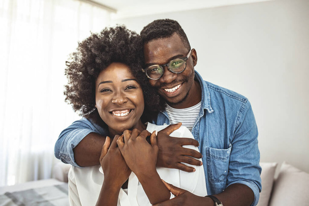 Portrait of a happy young couple at home. Portrait of happy couple looking at camera against gray background. Enjoying every minute together. Cropped portrait of a man affectionately embracing his wife at home - Photo, image
