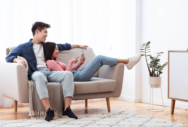 Asian Couple Using Smartphone Sitting On Sofa At Home - Photo, Image