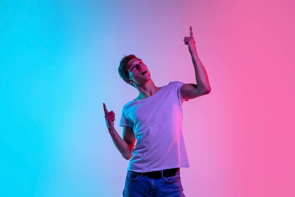 Young caucasian mans portrait on gradient blue-pink studio background in neon light - Фото, зображення