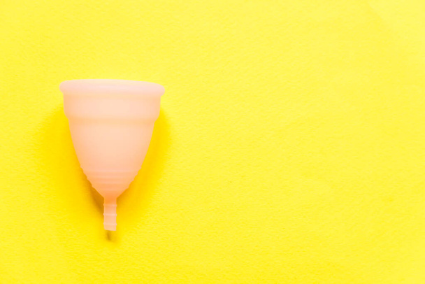 Simpelweg minimaal design roze menstruatiecup Geïsoleerd op gele achtergrond. Vrouw moderne alternatieve eco gynaecologische hygiëne in de menstruatieperiode. Een container voor bloed. Flat lay bovenaanzicht kopieerruimte - Foto, afbeelding