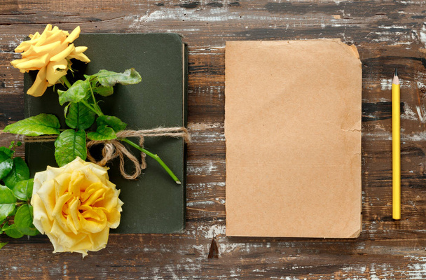 Bouquet of beautiful yellow roses and stack of books on wooden background. A sheet of paper and pencil. - Foto, Bild