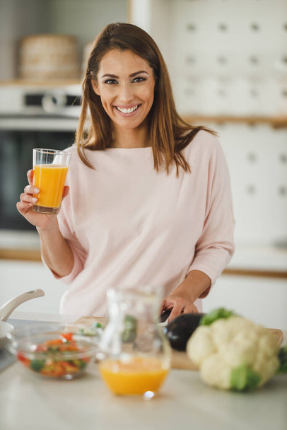 Girato di una giovane donna che beve succo d'arancia fresco nella sua cucina. - Foto, immagini