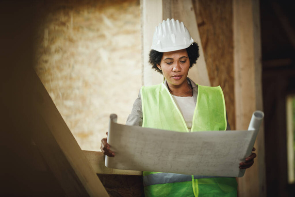 Застрелений африканською жінкою-архітекторкою, він перевіряє плани на місці будівництва нового дерев'яного будинку. Вона носить захисні робочі костюми і білий шолом.. - Фото, зображення