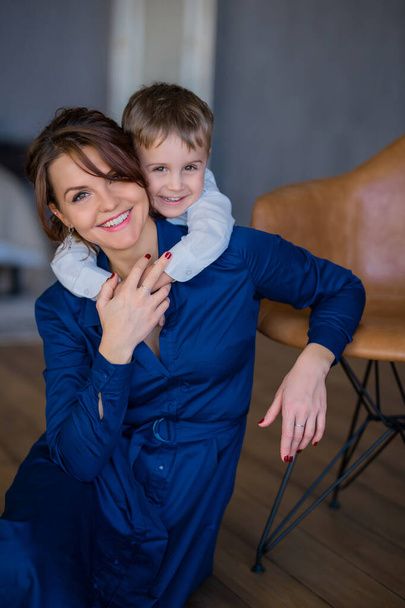 beautiful mother in a dress sits on the floor and her son hugs - Фото, зображення