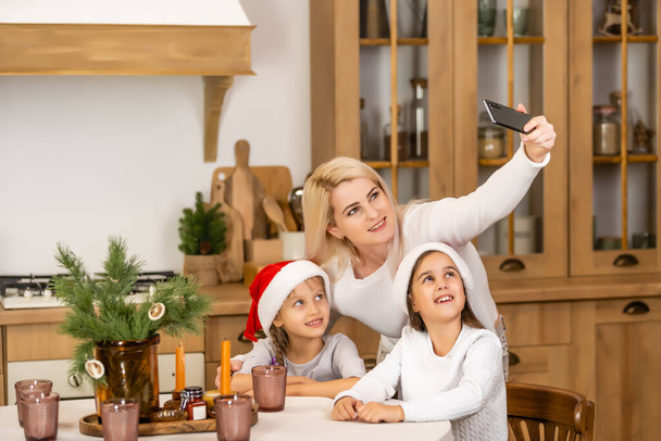 Noël en ligne félicitations à la famille. Souriant européenne blonde mère et fille faisant selfie photo dans les costumes de Noël maison - Photo, image