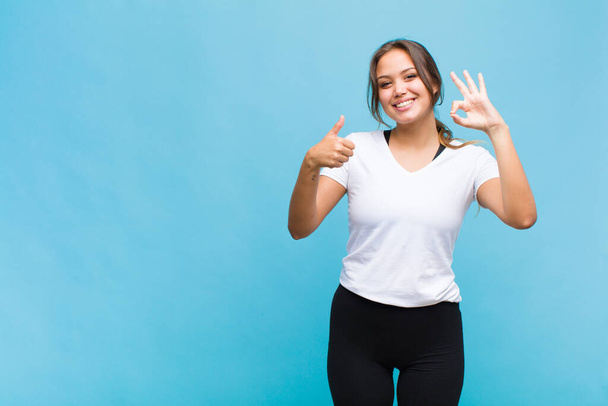 young hispanic woman feeling happy, amazed, satisfied and surprised, showing okay and thumbs up gestures, smiling - Foto, afbeelding