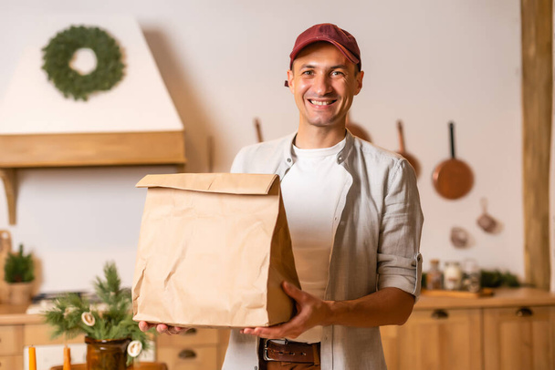 un repartidor con un paquete de comida se encuentra en un interior de Navidad - Foto, Imagen