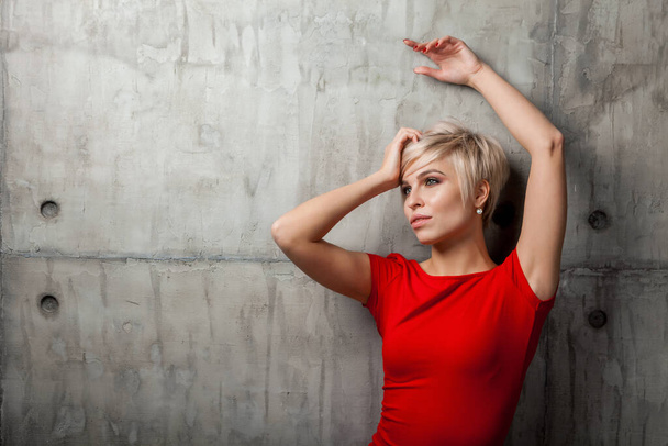 Blonde woman with a short haircut in a red dress against the background of the old wall - Фото, зображення