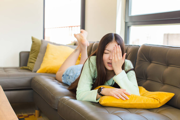 young asian woman looking sleepy, bored and yawning, with a headache and one hand covering half the face - Photo, image