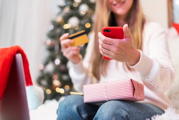 Close up of woman hands with mobile phone, credit card, gifts and laptop. Online shopping at Christmas holidays. Freelance girl woking from home office - Photo, Image