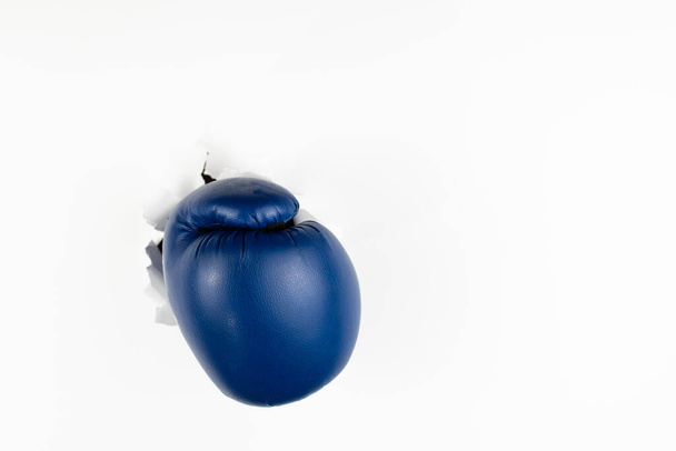 Un gant de boxe bleu traverse un mur de papier blanc. Le concept de réussite par des obstacles. Espace libre pour le texte. - Photo, image