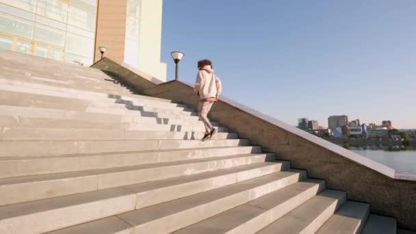 Slow-motion full back-view shot van slanke vrouwelijke jogger doet 's morgens cardiotraining gaat de trap op in het centrum van de stad bij daglicht - Video