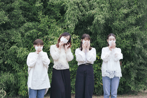 Vier jonge japanse vrouwen dragen witte shirts en maskers buiten - Foto, afbeelding