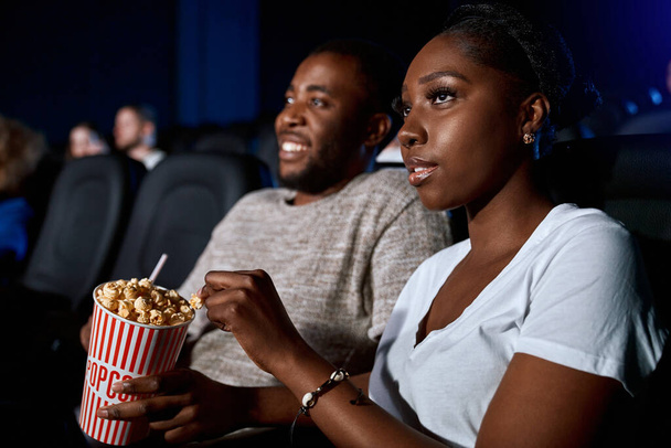 African couple eating popcorn in cinema. - Фото, зображення