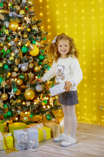 little girl near the Christmas tree holding a gift smiling  - Foto, Imagen