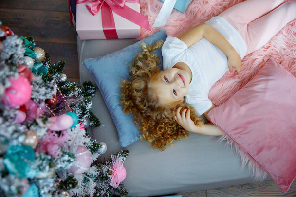 una bambina vicino all'albero di Natale è sdraiata sul letto - Foto, immagini