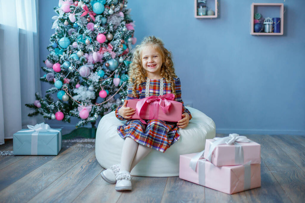 маленька дівчинка біля ялинки тримає подарунок усміхнений
 - Фото, зображення