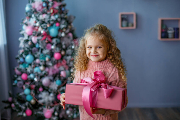 holčička v blízkosti vánočního stromečku drží dárek s úsměvem - Fotografie, Obrázek