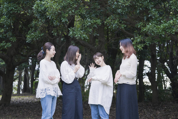 4 giovani donne giapponesi che indossano camicie bianche e chattano nel parco - Foto, immagini