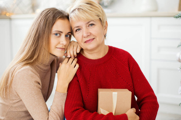 Beautiful mother and mature daughter at home near the Christmas tree. Christmas concept. - Photo, image