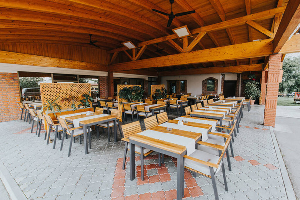 An outdoor restaurant with a wooden roof surrounded by trees at daytime - Fotó, kép