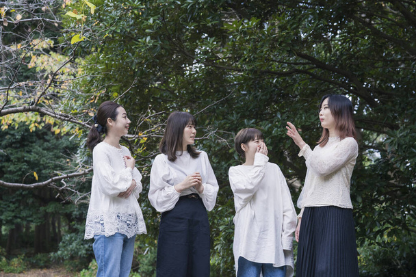 4 Japanse jonge vrouwen dragen witte shirts en chatten in het park - Foto, afbeelding