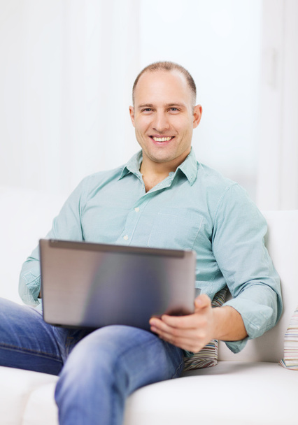 Smiling man working with laptop at home - Фото, изображение