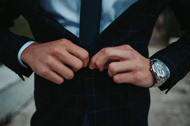 A closeup of a person buttoning a suit jacket while walking through a park - Foto, immagini
