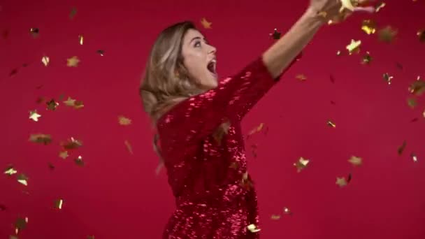 Zeitlupe einer fröhlichen Frau, die sich in der Nähe fallender Konfetti auf rotem Hintergrund dreht  - Filmmaterial, Video