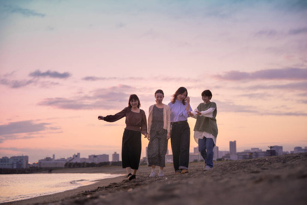 Τέσσερις νεαρές γυναίκες περπατούν κατά μήκος της θάλασσας το σούρουπο - Φωτογραφία, εικόνα