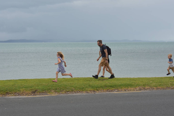 AUCKLAND, NEW ZEALAND - Nov 08, 2020: View of father and kids running on beach when rain starts - Foto, Imagen