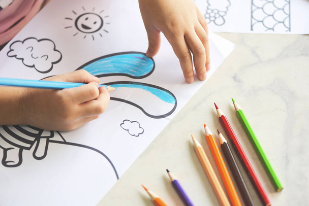 Дитяча дівчинка малює на паперовому листі з кольоровими олівцями на дерев'яному столі вдома / Дізнайтеся, як дитина малює картину і барвистий креон
 - Фото, зображення