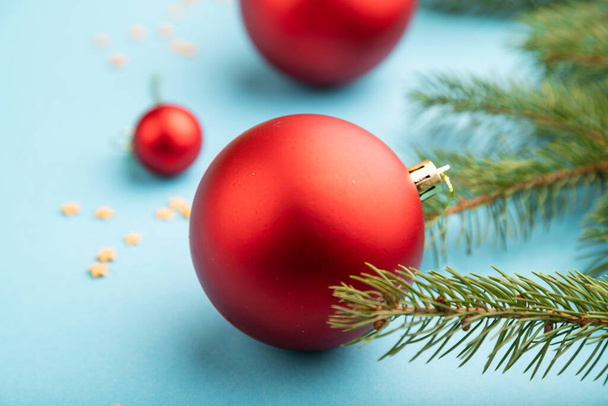 クリスマスまたは新年の組成物。青い紙の背景に装飾、赤いボール、モミやトウヒの枝。サイドビュー、コピースペース. - 写真・画像