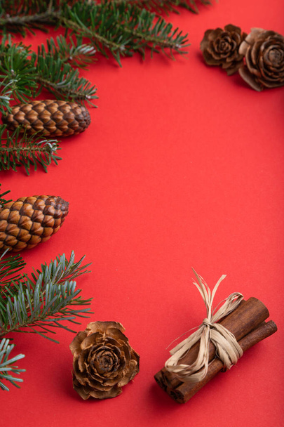 Kerst of nieuwjaarscompositie. Decoraties, doos, kaneel, kegels, sparren en sparren takken, kopje koffie, op een rode papieren achtergrond. Zijaanzicht, kopieerruimte. - Foto, afbeelding