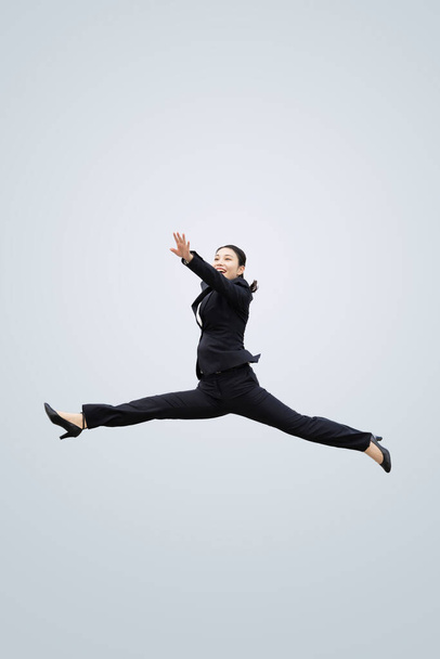 Een jonge zakenvrouw in een pak springt met een glimlach - Foto, afbeelding