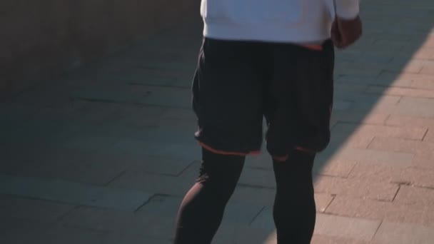 Tilting-up slow motion back-view beelden van jonge fitte man in compressie sport set joggen op zonnige ochtend met prachtig uitzicht op de stad - Video