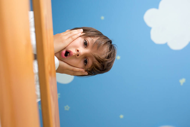 Funny portrait of a cute child, boy, looking from a double  deck bed down, sky and clouds painted on the ceiling - Photo, image