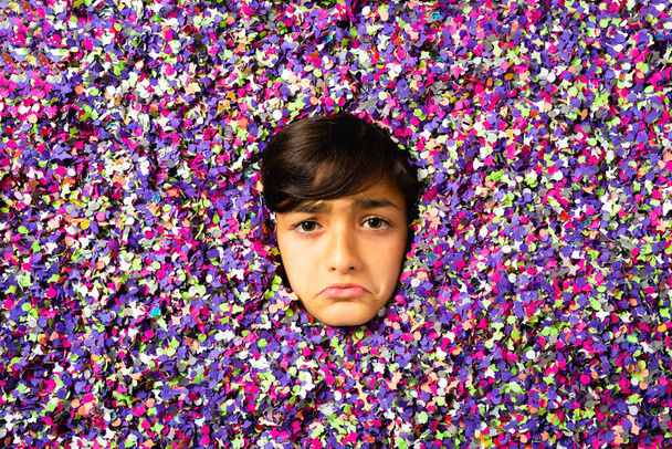 młody chłopiec smutny twarz jest otoczony kolorowe confetti - Zdjęcie, obraz