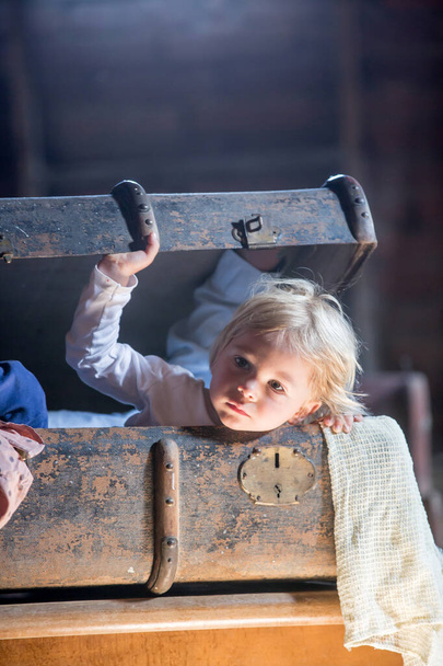 Little child, boy, hiding in old vintage suitcase in the attic, scared not to be found - Foto, Imagem