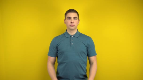 A young man makes a sad smile on her face with his fingers on a yellow background. Man in a green polo. - Footage, Video