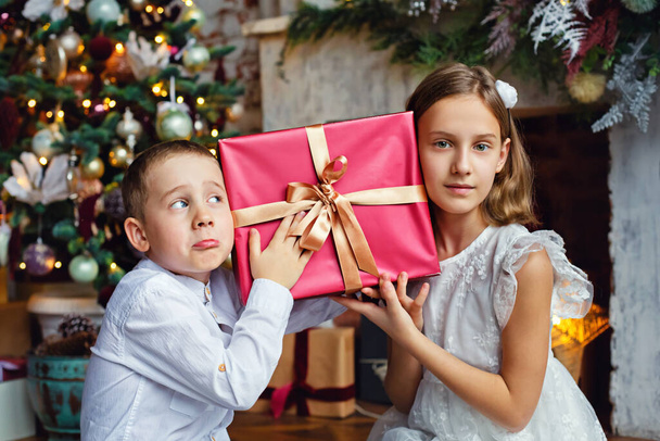 Děti otevírají vánoční dárky. Děti pod vánoční stromeček s dárkovými krabicemi. Zdobený obývací pokoj s tradičním krbem. Útulný teplý zimní den doma. - Fotografie, Obrázek