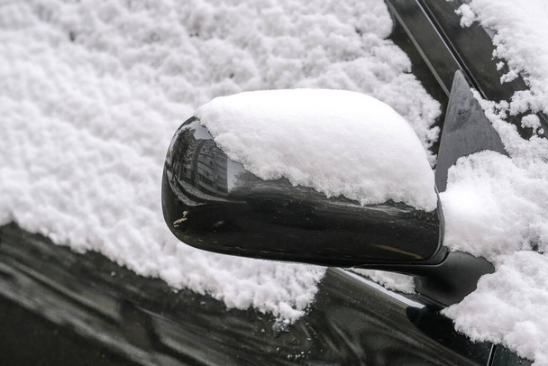 Um carro de passageiros preto está estacionado perto de um edifício residencial na cidade coberto com o primeiro fragmento de close-up de neve de outono - Foto, Imagem