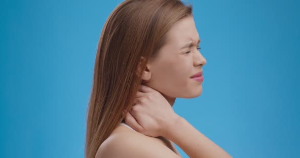 Боль в шее. Уставшая женщина с болезненными чувствами в мышцах шеи, синий студийный фон - Кадры, видео