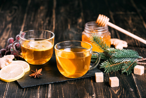 Bicchiere di tè caldo allo zenzero con limone e miele sul tavolo di legno scuro. Limoni affettati su un tagliere di pietra - Foto, immagini