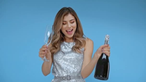 Veselá žena drží sklo a láhev šampaňského izolované na modré  - Záběry, video